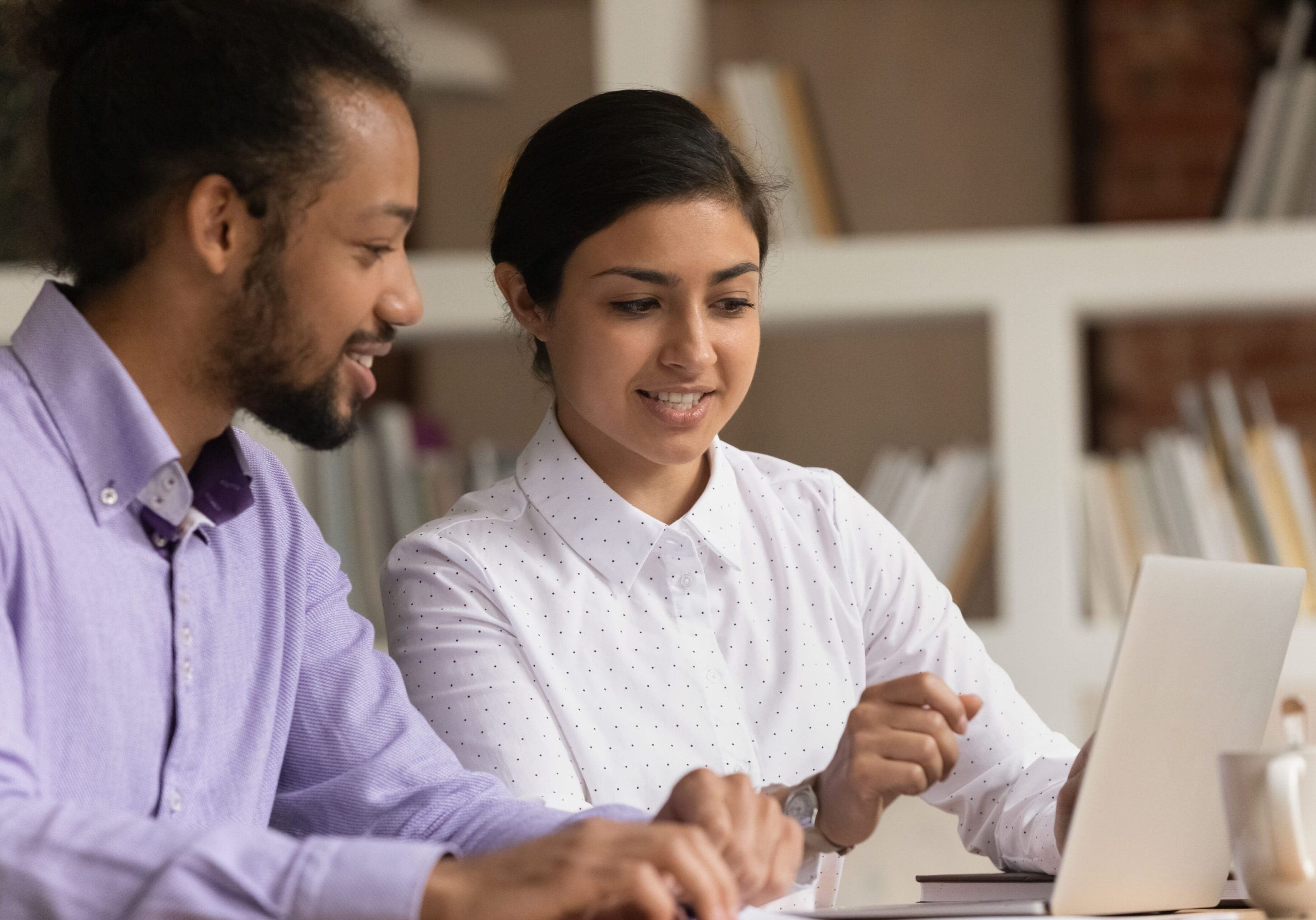 A man and woman sitting at a table looking at a laptop.